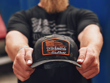 Load image into Gallery viewer, "We The Essentials" Multicam Black Trucker Hat with Orange Patch